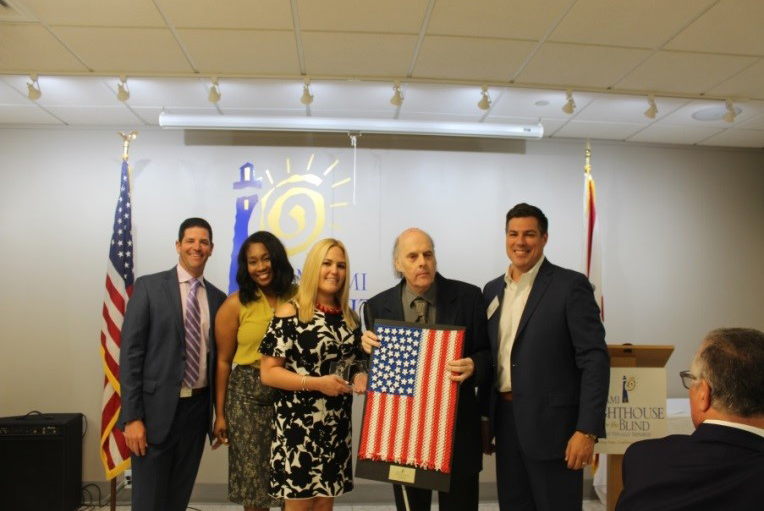 Miami Lighthouse Senior Group Activities client Victor and YPOL Co-Chair Alex Suarez presents handmade American Flag to luncheon sponsor AT&T represented by Cristal Cole, Thais Asper and Alex Dominguez